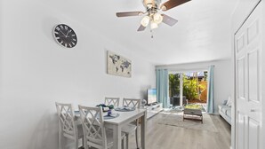 A dining area with a white table and chairs, a ceiling fan, a world map artwork, and a view of the outdoors through a glass door.