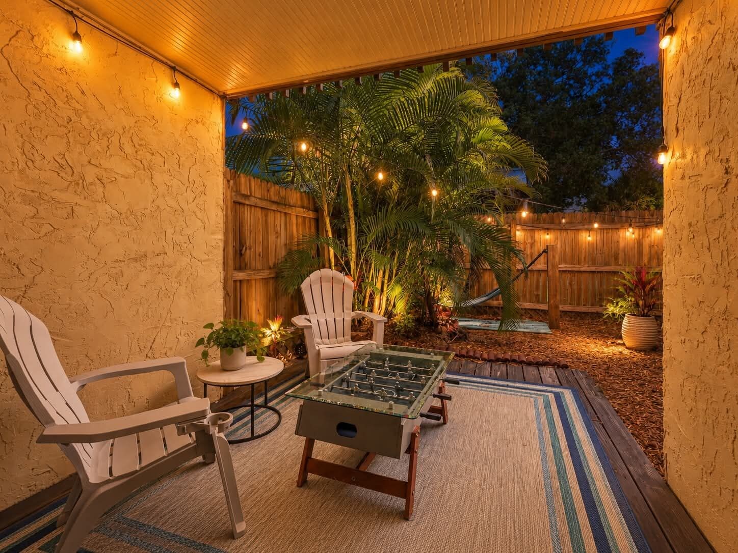 An outdoor patio area with a foosball table, two chairs, and string lights.