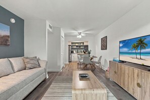 A modern living room with a sofa, coffee table, TV, and a kitchen in the background.