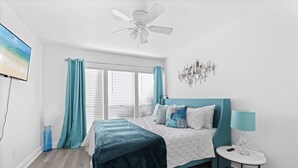 A bedroom with a bed, a ceiling fan, a TV, and a window with curtains.