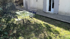 Un patio con mesa y sillas de vidrio, rodeado de follaje y un muro de piedra.