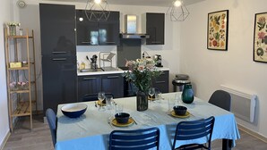 Una cocina moderna con armarios oscuros, una mesa de comedor con sillas azules y dos lámparas colgantes.