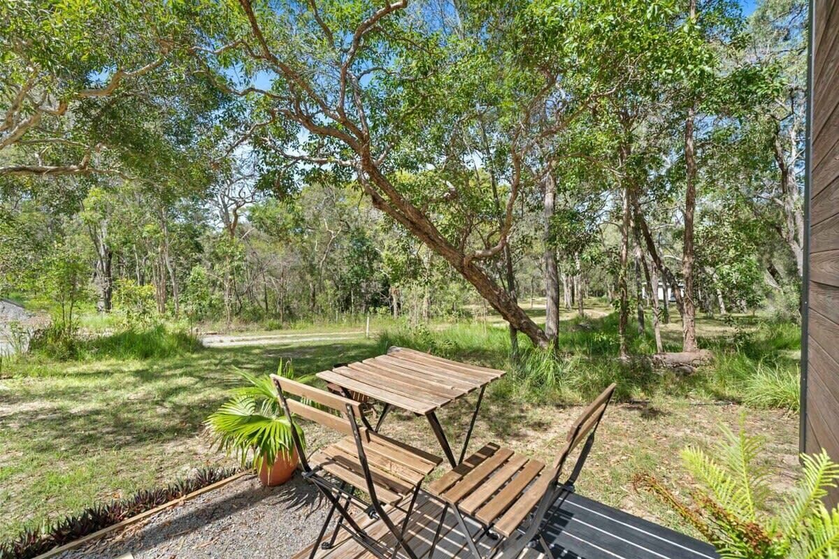 An outdoor patio with a wooden table and chairs, surrounded by trees and greenery.