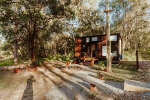Une cabane dotée d’une terrasse en bois, entourée d’arbres et de plantes en pot.
