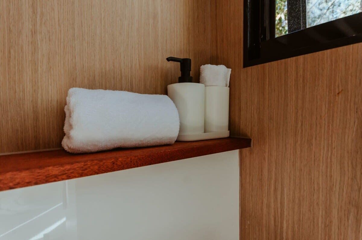 A bathroom with a wooden wall, a white towel, and a soap dispenser on a shelf.