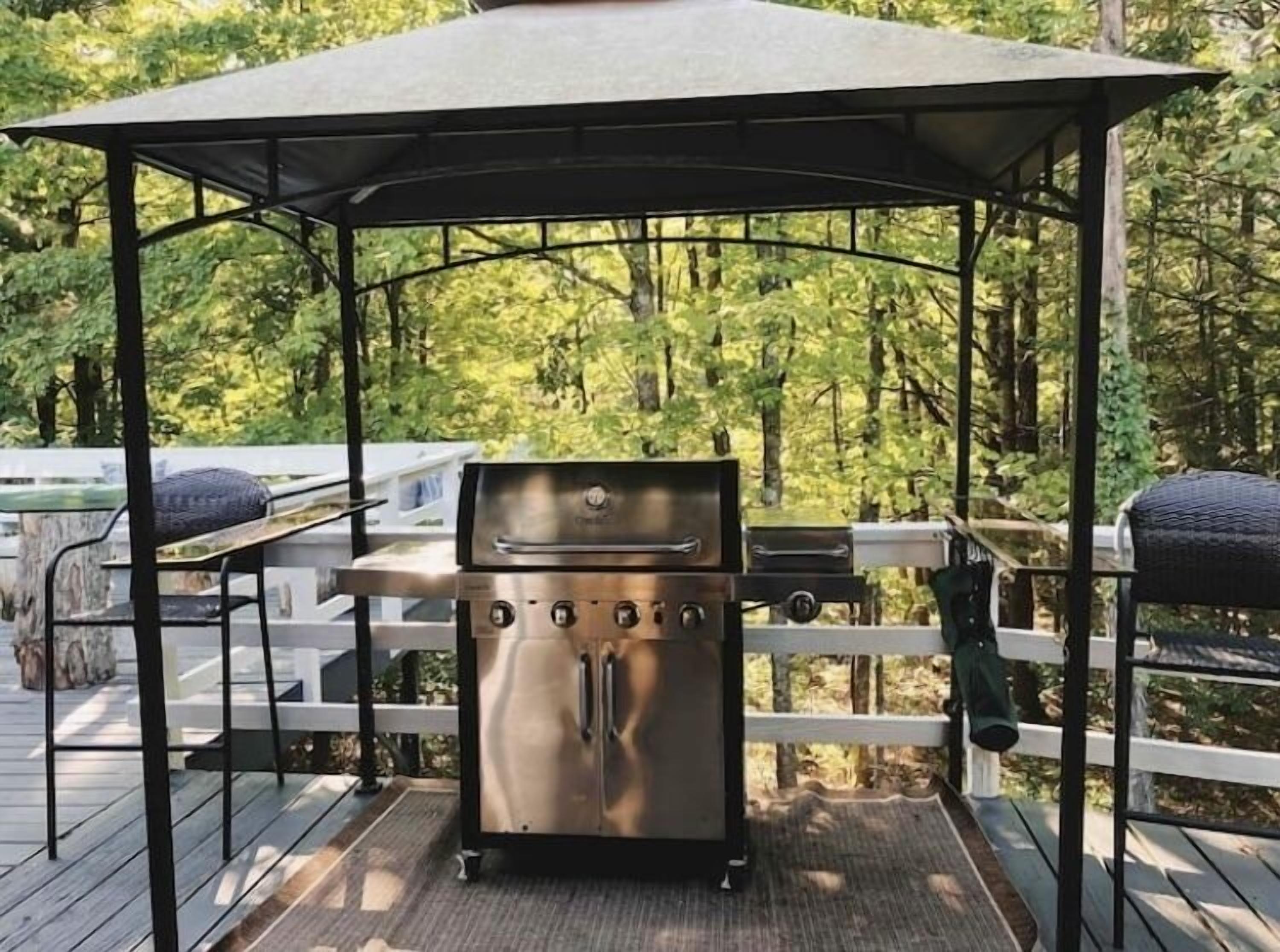 A barbecue grill under a gazebo on a wooden deck with a forest backdrop.