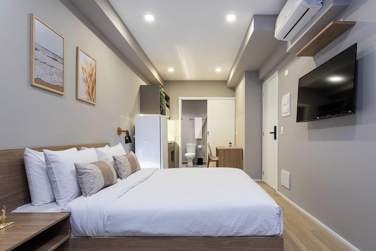 Ein Schlafzimmer mit einem Bett, einem Fernseher, einer Klimaanlage und einem durch eine offene Tür einsehbaren Badezimmer.