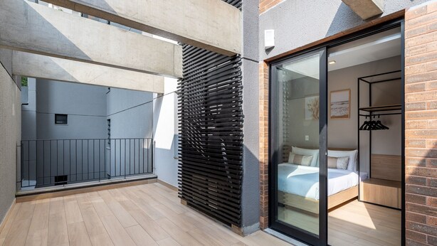 Een moderne hotelkamer met een grote schuifglazen deur, een bed, een houten bankje en een metalen plank.
