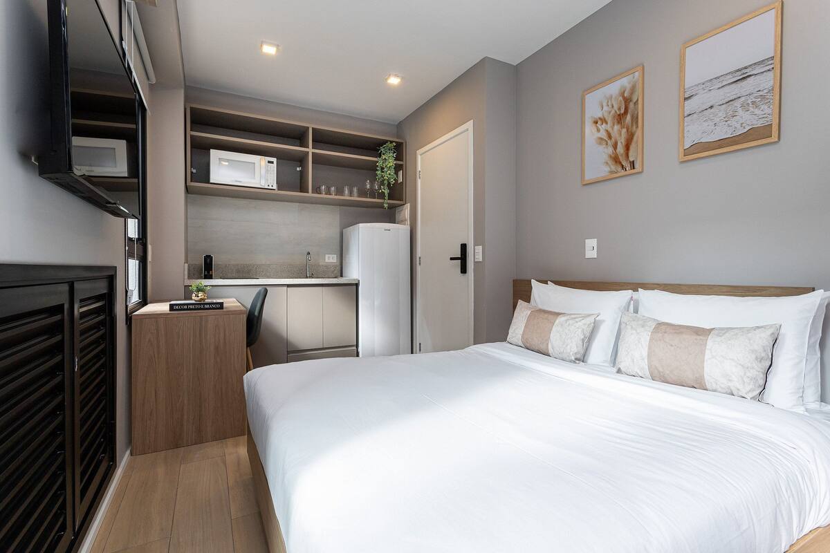 Une chambre avec un lit, une petite kitchenette et une porte donnant sur une autre pièce.