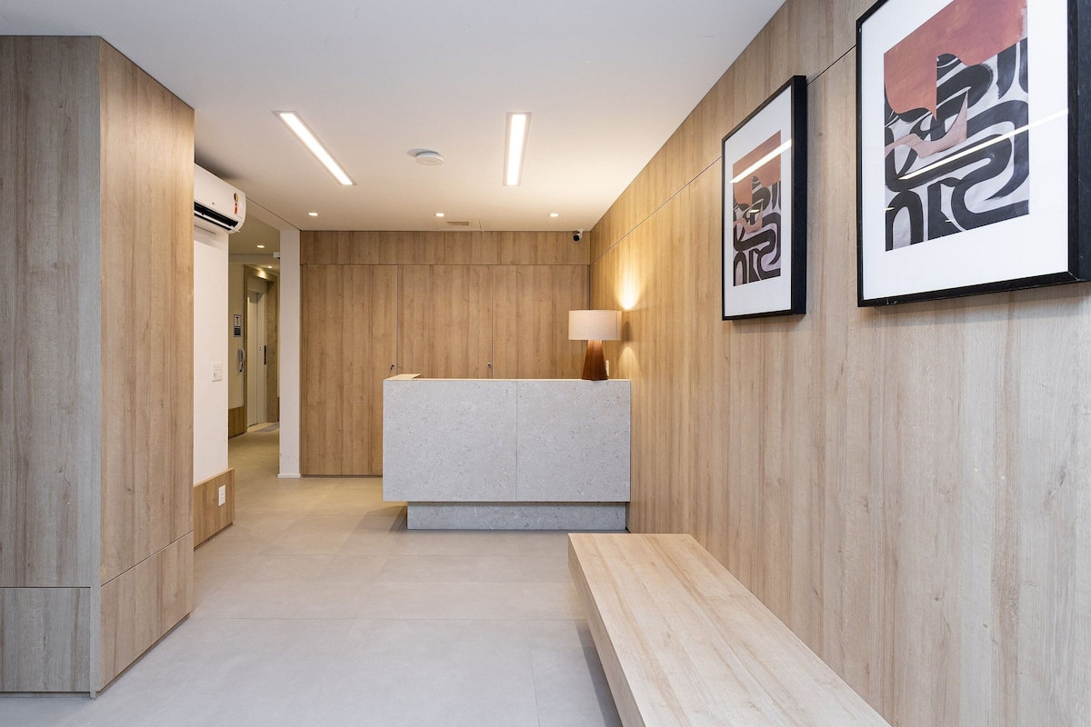 Un espace d’accueil moderne avec un comptoir de réception en bois, un banc et des œuvres d’art encadrées accrochées au mur.