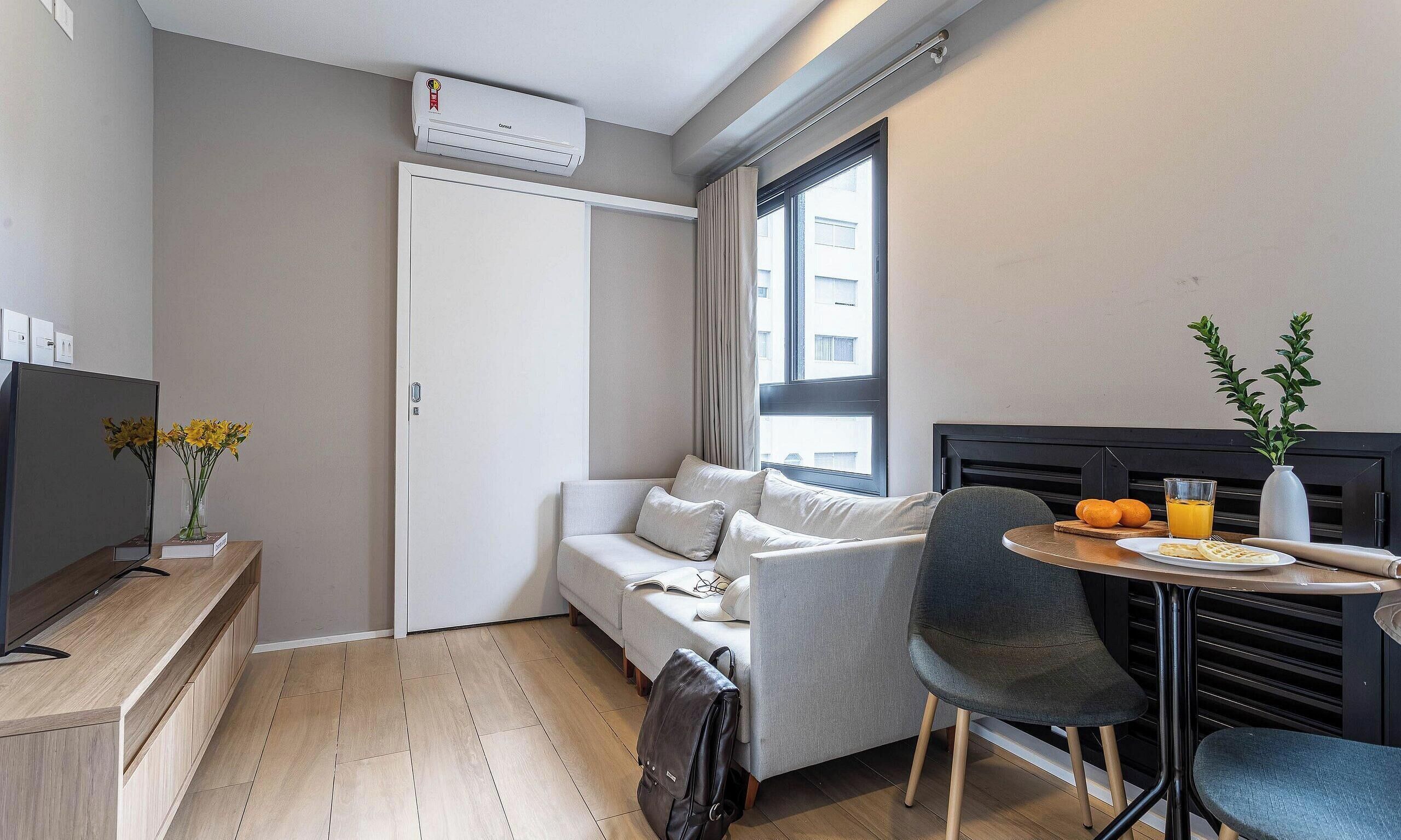A compact living space with a sofa, a dining table with a chair, a TV, and a window with curtains.