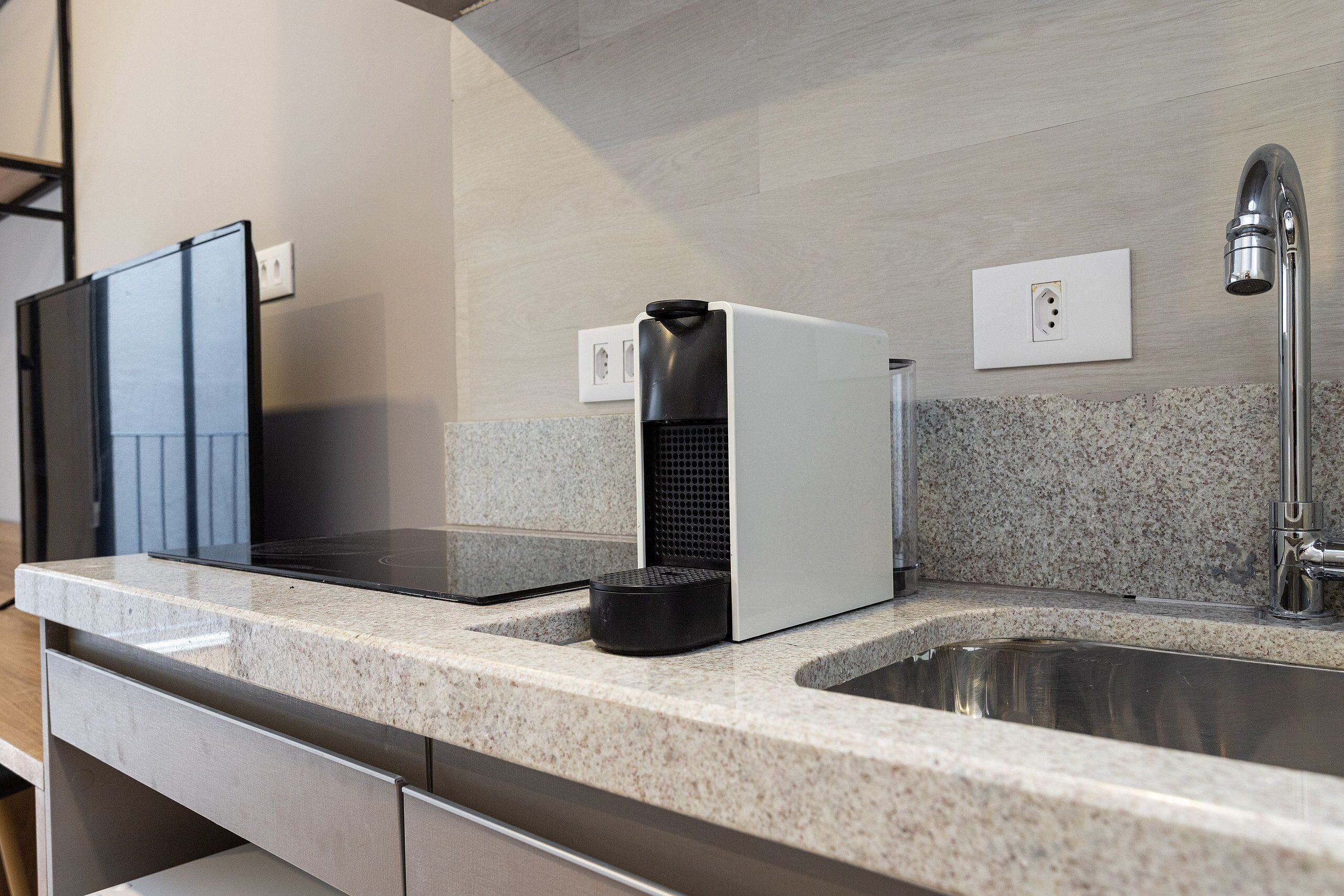 A modern kitchen with granite countertops, a stainless steel sink, a black coffee maker, and a white appliance.