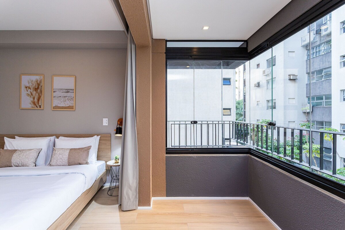 A bedroom with a bed, a nightstand, a window, and a balcony.