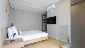 Een moderne slaapkamer met een bed, nachtkastje, lamp, airconditioning en een kledingkast.