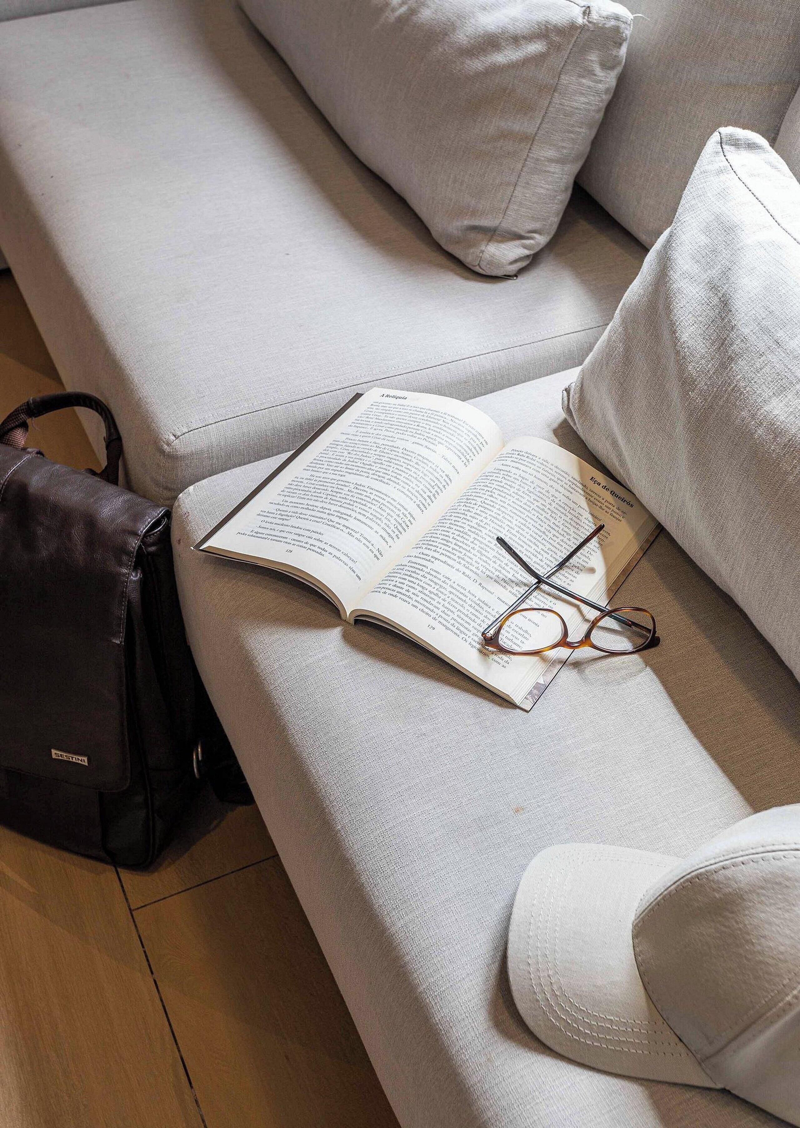 A book, glasses, and a black bag on a light-colored sofa.