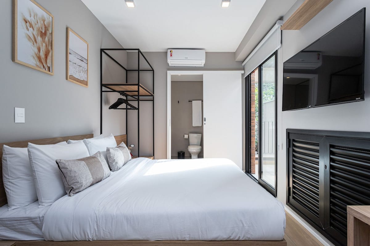 Une chambre moderne dotée d’un grand lit, d’étagères intégrées, d’un climatiseur, d’un téléviseur et donnant sur l’extérieur grâce à une porte coulissante.