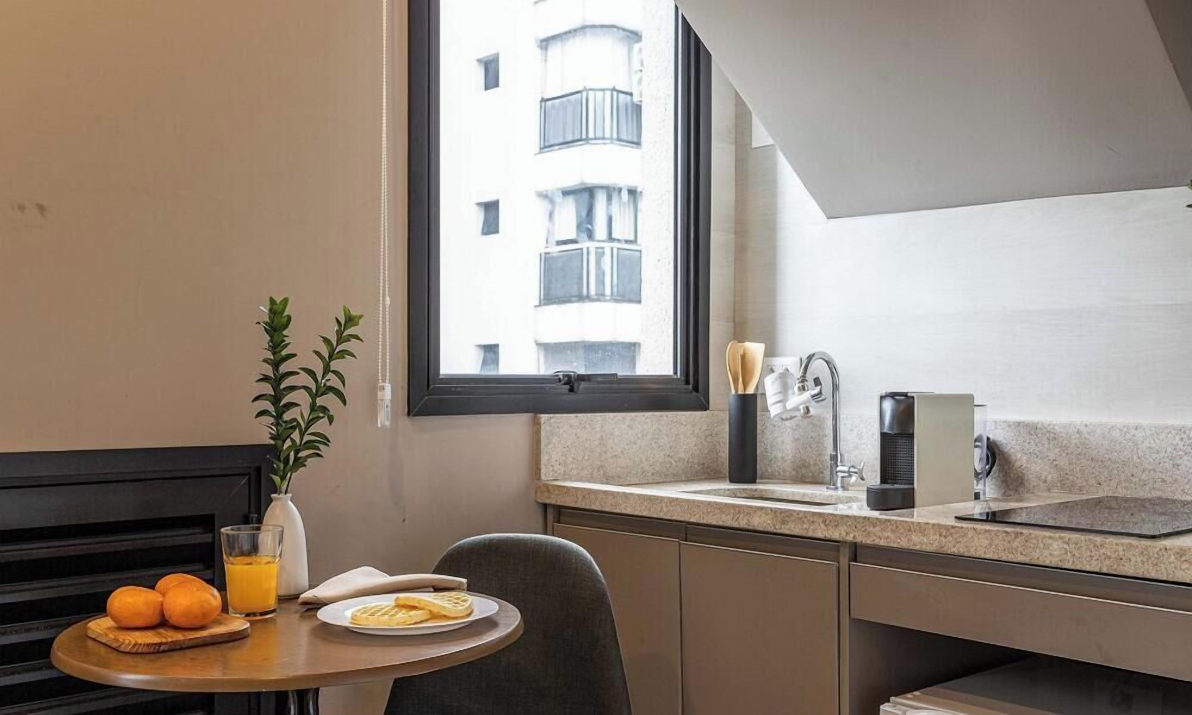 A compact kitchenette with a window, a sink, and a small dining area with a table set for breakfast.