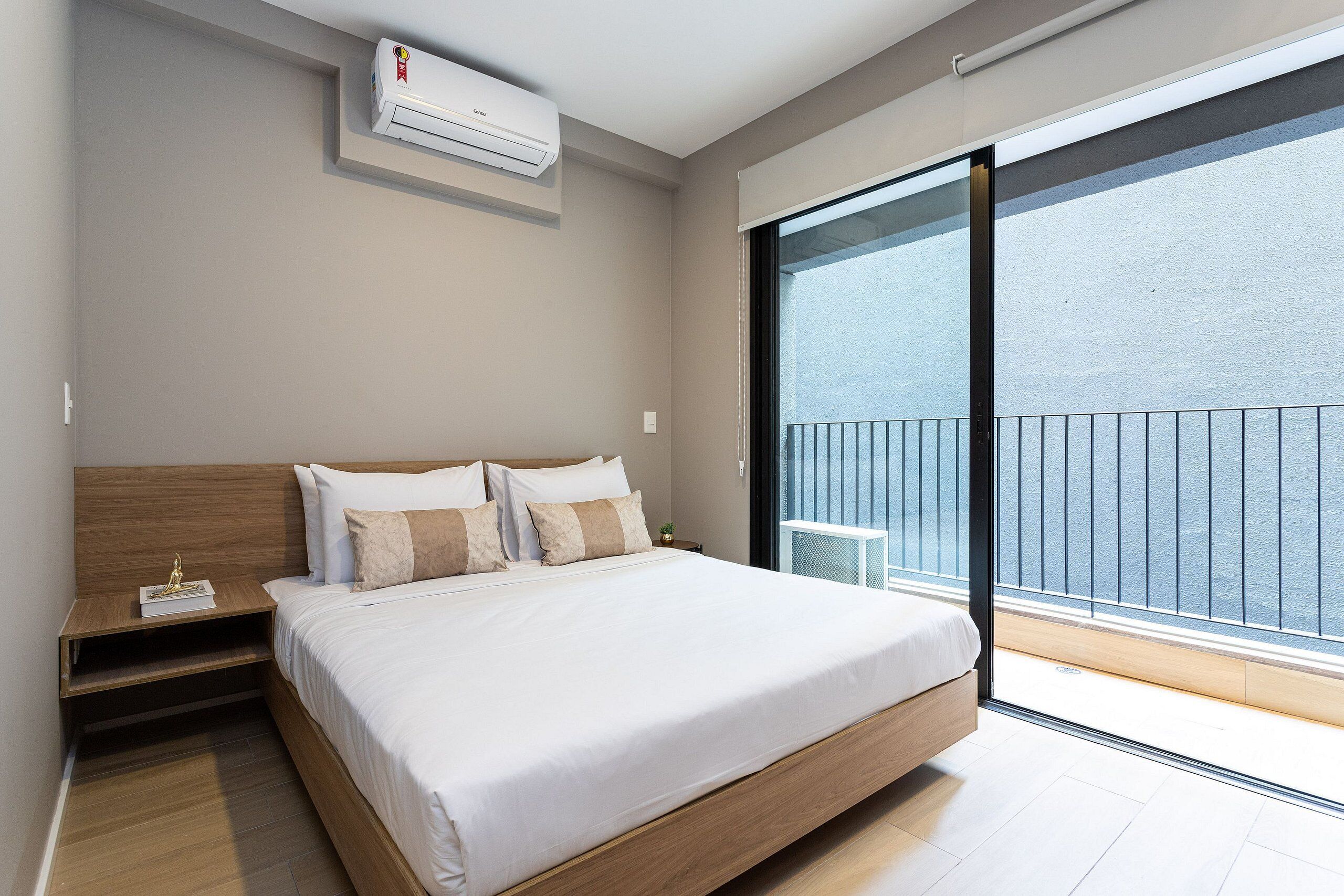 A modern bedroom with a large bed, a nightstand, a small table, and a view of the outside through a sliding door.
