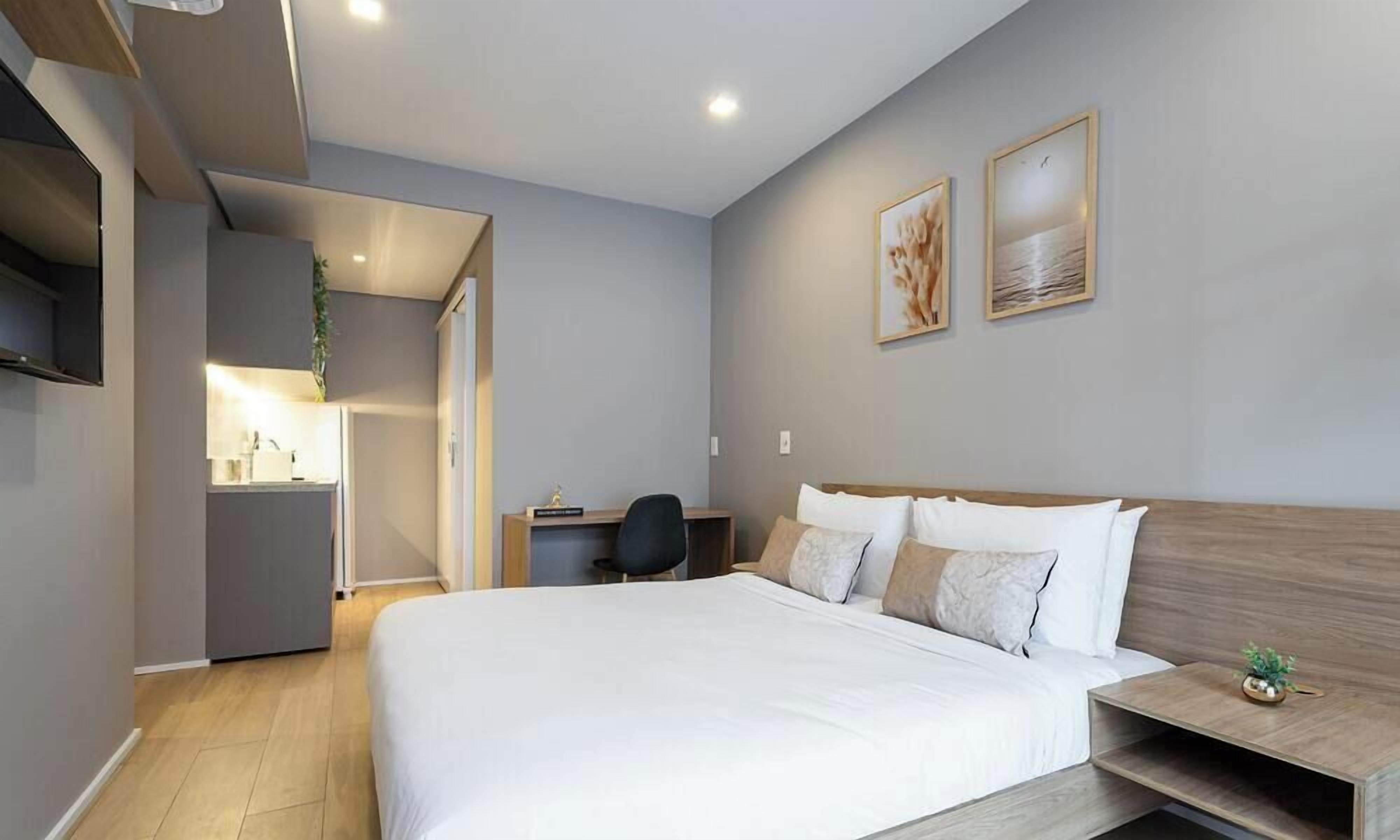 A modern hotel room with a large bed, a desk, and a small seating area.