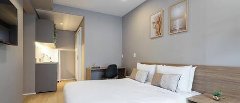 A modern hotel room with a large bed, a desk, and a small seating area.