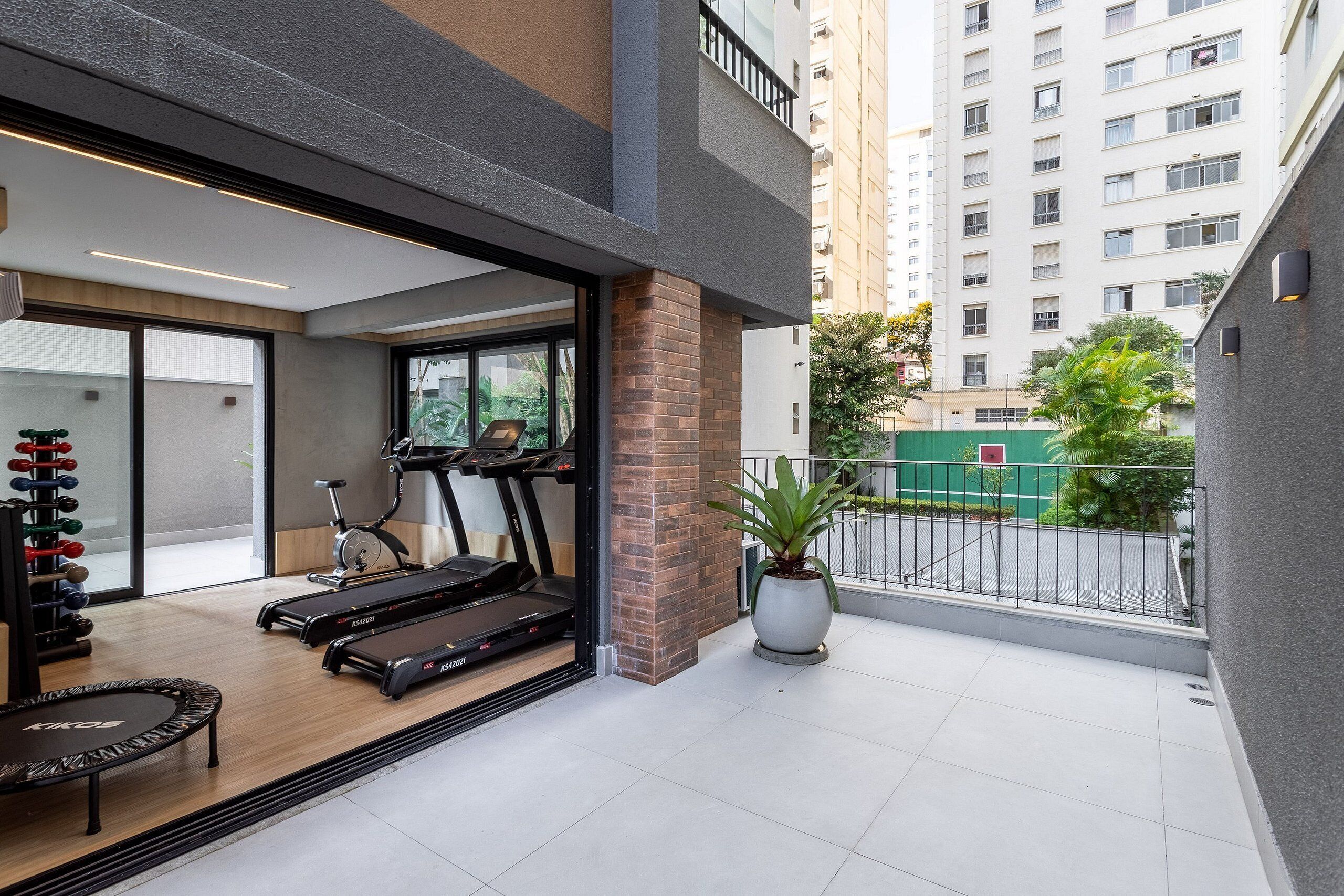 A modern apartment with a balcony, exercise equipment, and a view of a high-rise building.