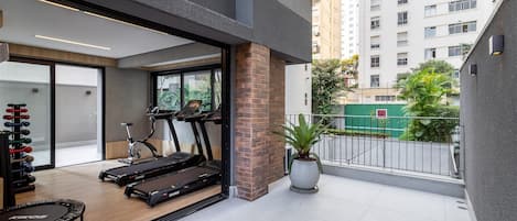 A modern apartment with a balcony, exercise equipment, and a view of a high-rise building.
