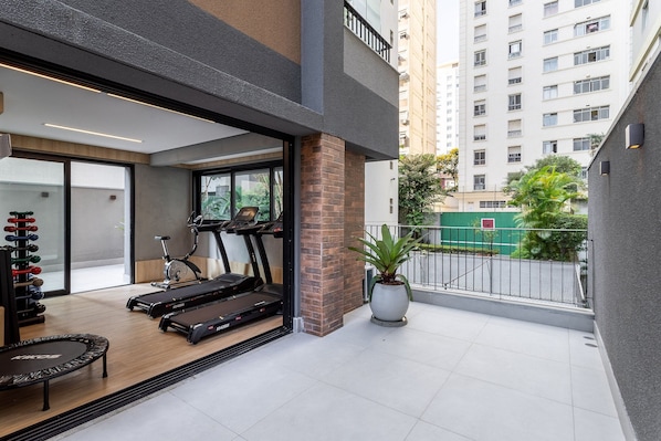 Un apartamento moderno con balcón, equipo de ejercicio y vistas a un edificio de gran altura.