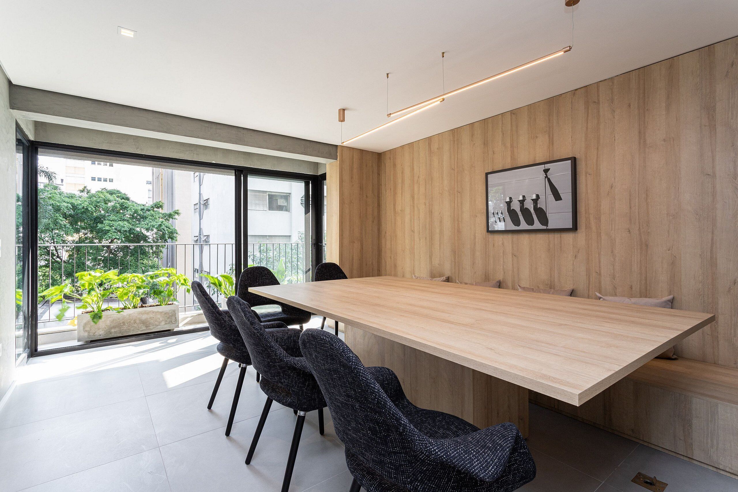 A modern meeting room with a long table, black chairs, a wooden accent wall, and a large window with a view of greenery.