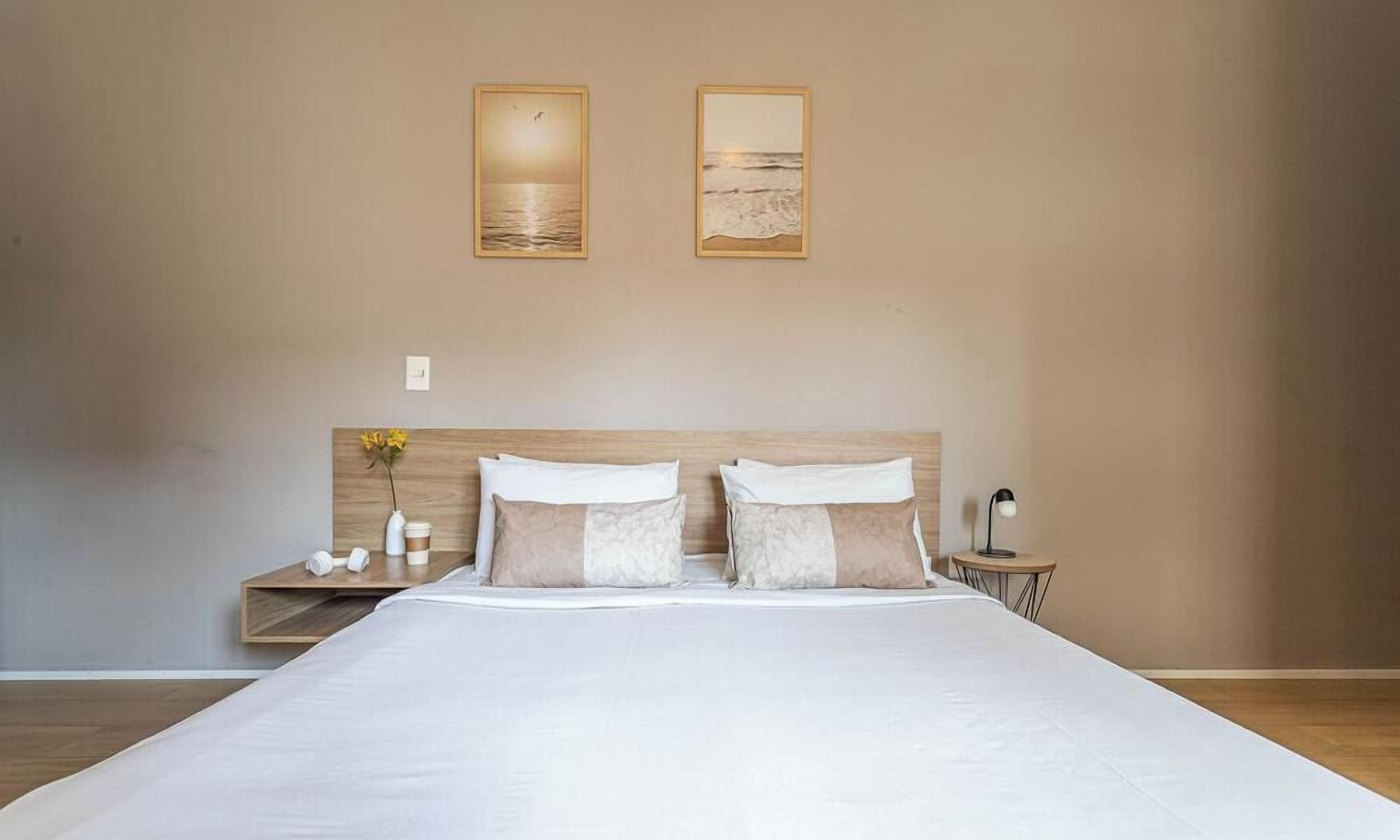 Un dormitorio con una cama grande, dos mesitas de noche y dos cuadros enmarcados en la pared.