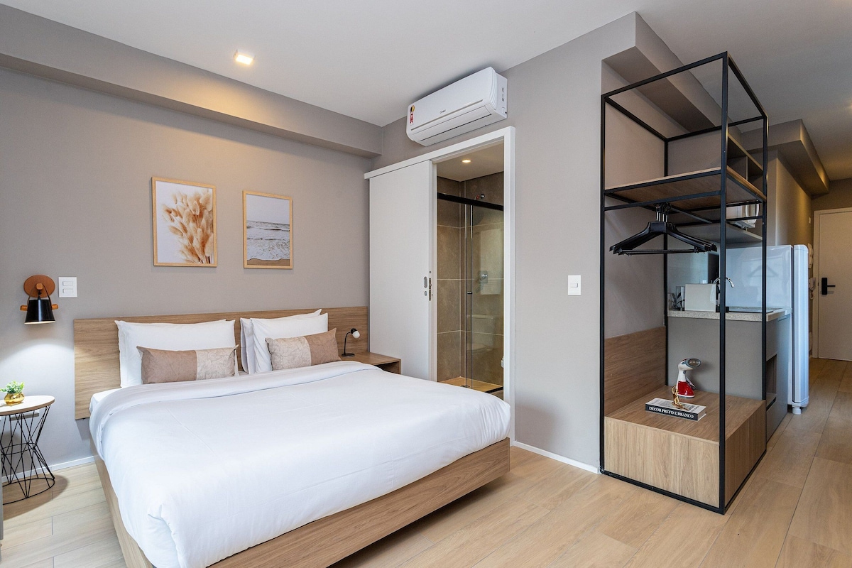 Ein modernes Hotelzimmer mit Bett, begehbarem Kleiderschrank und einer Duschkabine aus Glas.