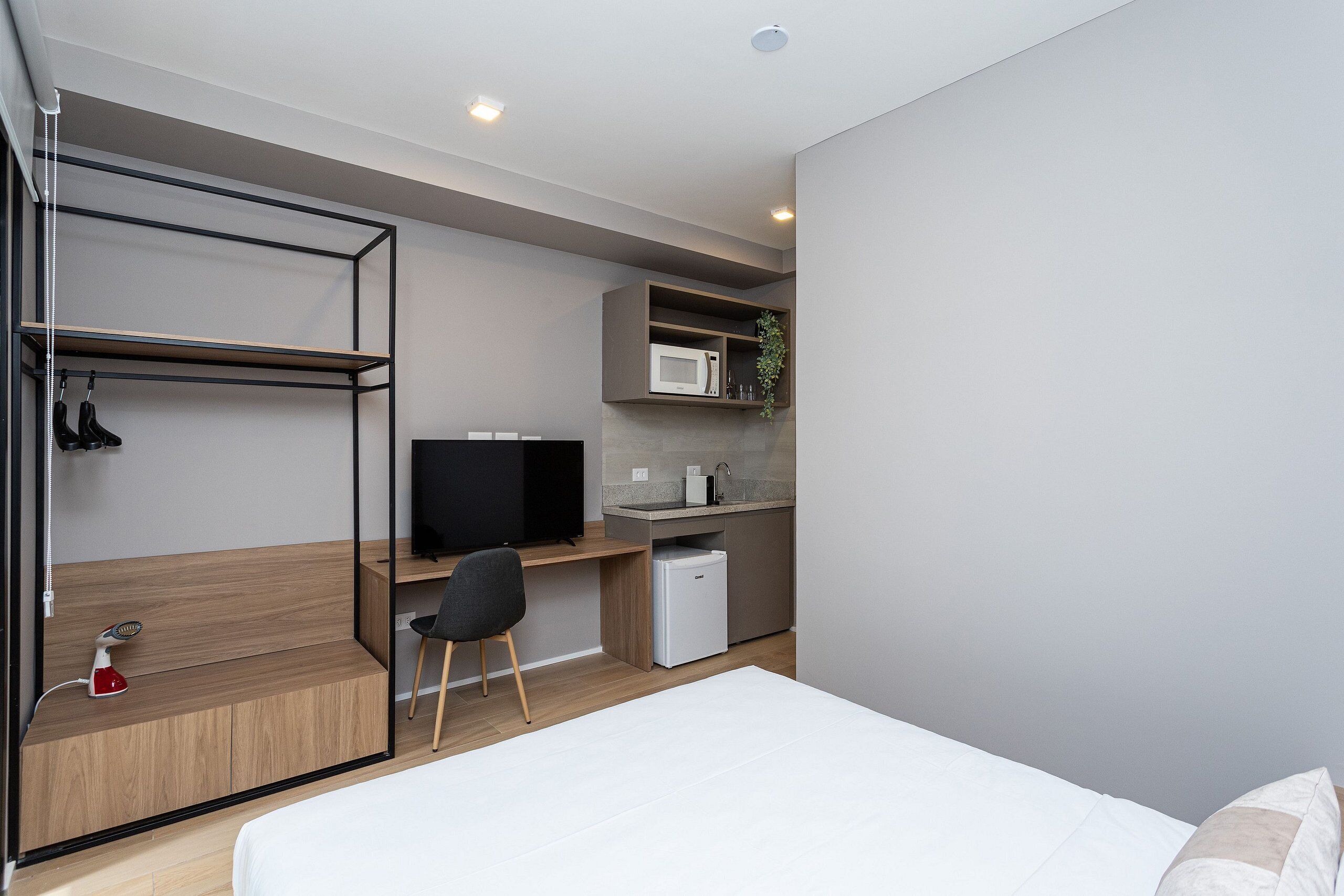 A compact room with a bed, a desk with a computer, a microwave, and a small refrigerator.
