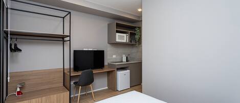 A compact room with a bed, a desk with a computer, a microwave, and a small refrigerator.