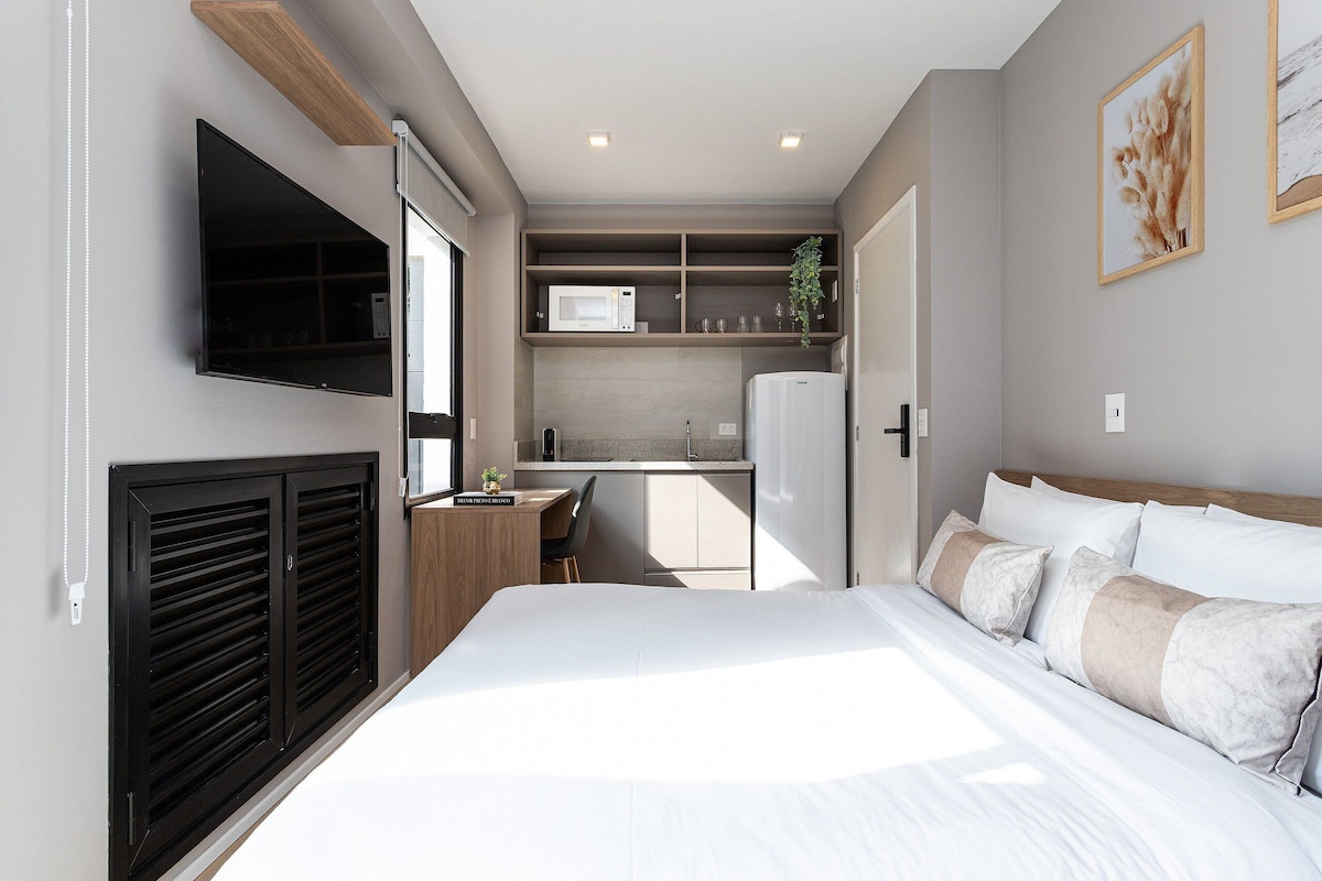 Ein kleines Hotelzimmer mit Bett, Schreibtisch, Mikrowelle und Fernseher.