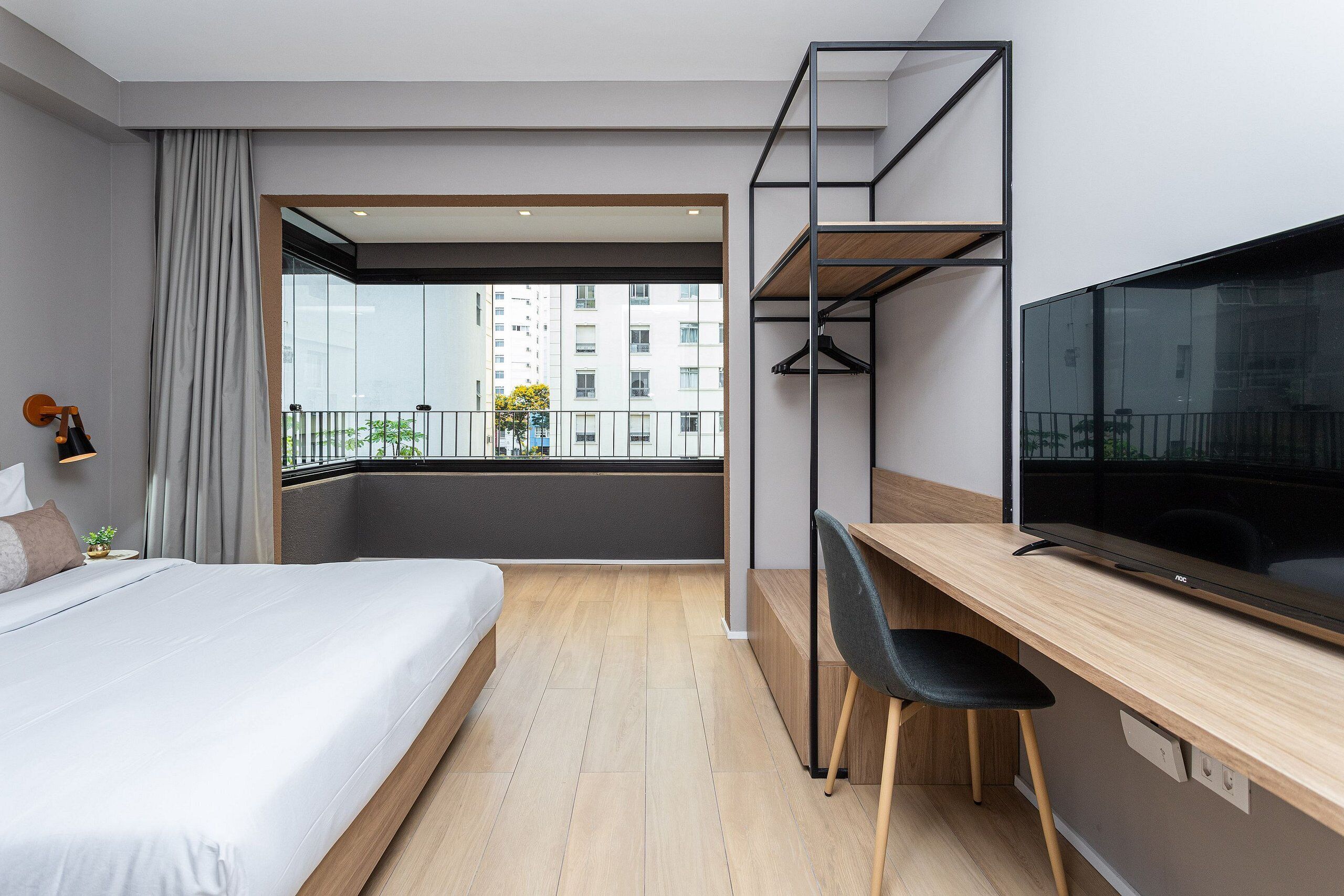 Ein modernes Hotelzimmer mit Bett, Schreibtisch, Stuhl, Fernseher und einem Balkon mit Blick auf die Stadt.