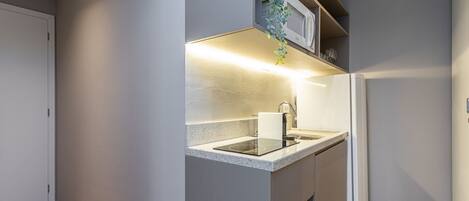 Cozinha moderna com micro-ondas embutido, pia de aço inoxidável e piso de madeira.