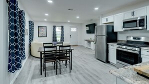A modern kitchen with white cabinets, stainless steel appliances, and a dining area with a table and chairs. - Step Into Paradise (River Oaks)