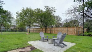 A backyard with a concrete patio, two Adirondack chairs, and a metal grill. - Step Into Paradise (River Oaks)