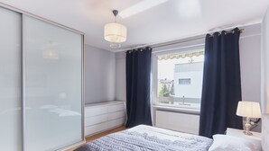 Une chambre à coucher avec un lit, une table de chevet avec une lampe, une fenêtre avec des rideaux, un radiateur et une armoire.