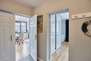 Stroll down the corridor to a dining area with a view of the outside, featuring a chair with a woven seat and a window with a curtain.