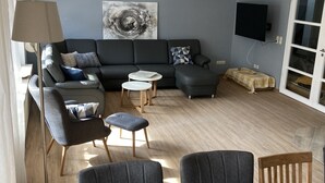 A modern living room with a sofa, armchairs, a coffee table, and a dining table with candles. - North Sea coast, charming Frisian house with fireplace, conservatory, sauna, beach chair (Wangerland)
