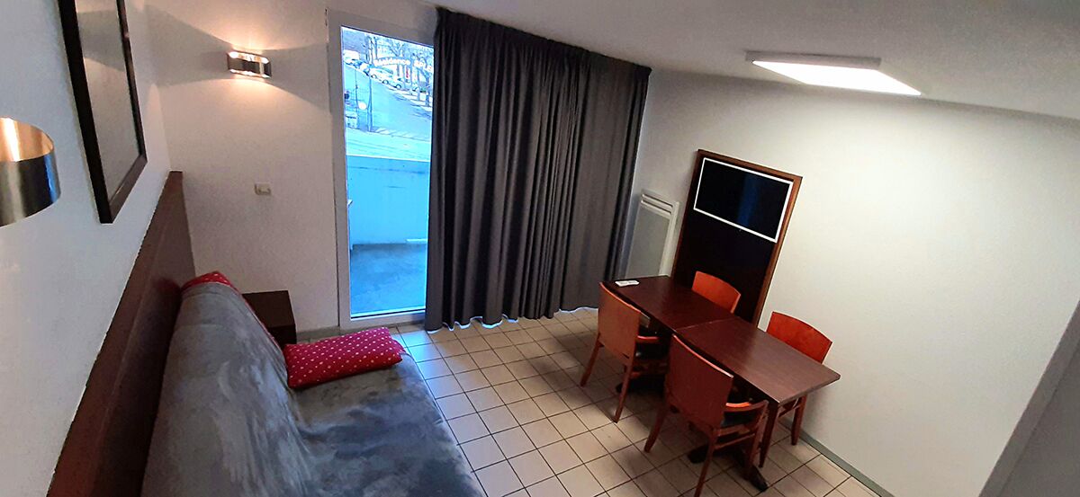 Ein Zimmer mit einer Couch, einem Esstisch mit Stühlen, einem Fernseher und einem Fenster mit Vorhängen.