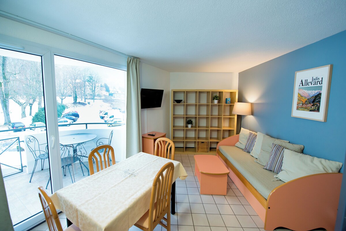 A room with a dining table, chairs, a sofa, a TV, and a bookshelf.