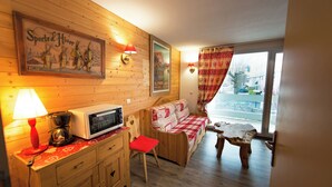 Interior acogedor de una cabaña con una pared de madera, un sofá, una mesita, un microondas y una lámpara.