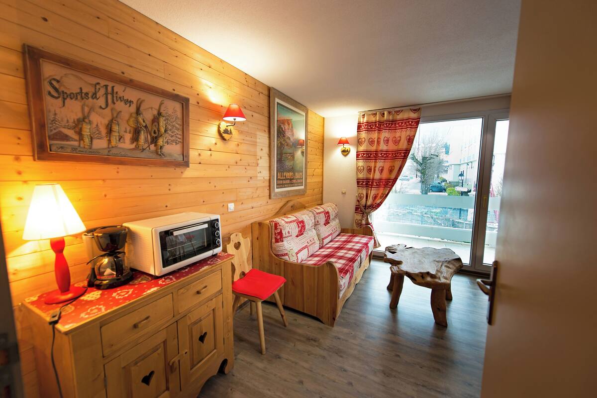 A cozy cabin interior with a wooden wall, a sofa, a small table, a microwave, and a lamp.