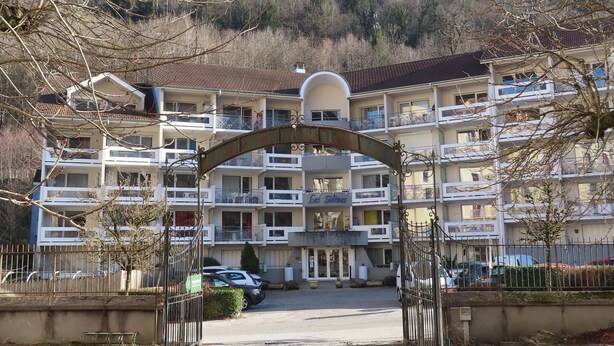 Un hotel de varios pisos con un acceso principal en forma de arco, balcones y un área de estacionamiento.