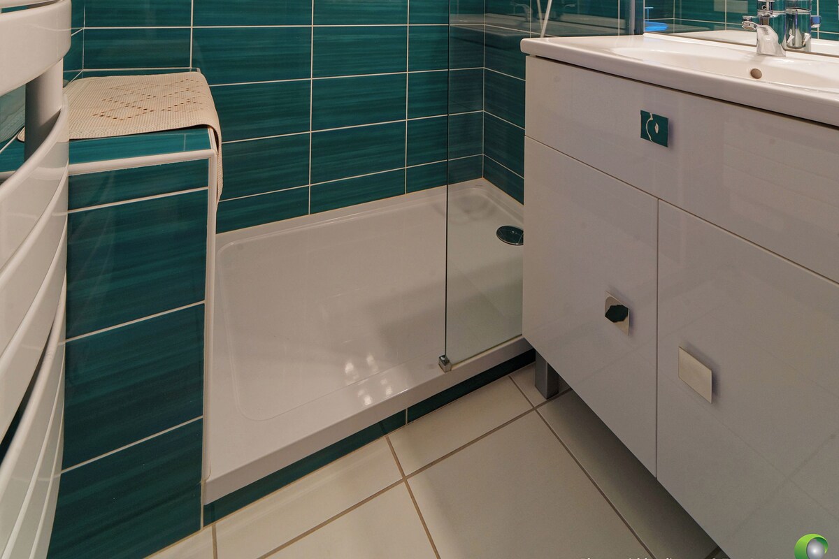 A modern bathroom with a glass shower enclosure, a white sink, and teal and white tiled walls.