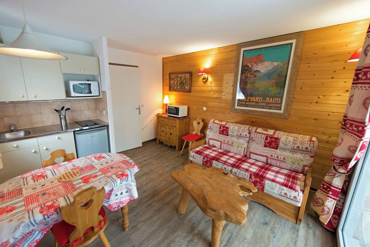 A cozy room with a wooden wall, a sofa, a wooden coffee table, a table with a checkered tablecloth, a microwave, a lamp, and a poster on the wall.