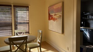 A dining area with a round table and two chairs, a window with blinds, and a kitchen area with shelves. - 3 bedroom Craftsman bungalow in the heart of Lakeland (Lakeland)