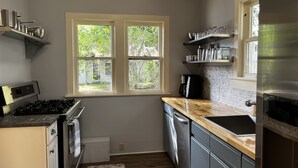 A modern kitchen with a gas stove, oven, dishwasher, and a window with a view of greenery. - 3 bedroom Craftsman bungalow in the heart of Lakeland (Lakeland)