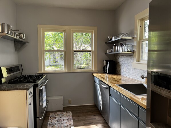 A modern kitchen with a gas stove, oven, dishwasher, and a window with a view of greenery.